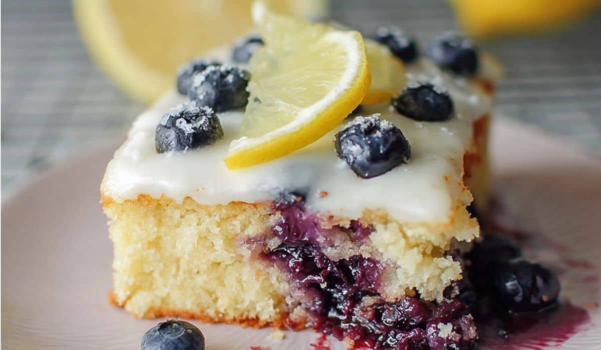 Moist lemon blueberry sheet cake slice with dripping glaze and fresh fruit