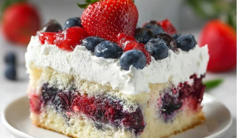 Close-up of a Summer Berry Poke Cake slice topped with whipped cream and fresh strawberries and blueberries