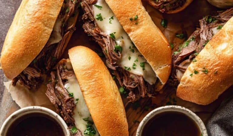 Crockpot French Dip Sandwiches on toasted rolls with bowls of au jus for dipping