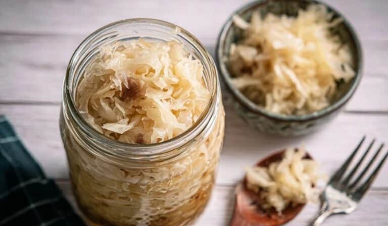 Jar of 5-day homemade sauerkraut with a small bowl of kraut on a rustic table