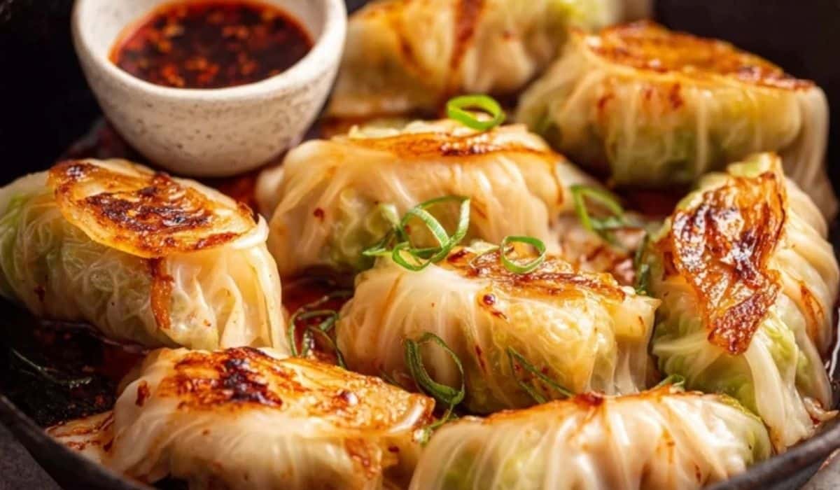 Korean-style cabbage rolls with chili oil in a skillet with sesame seeds and green onions